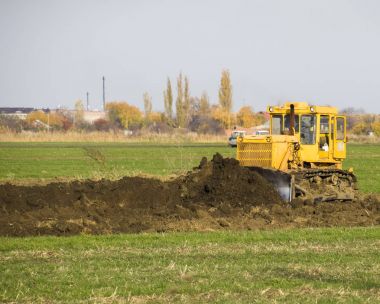 Sarı traktör ekli grederom ile zemin tesviye yapar. Drenaj sistemi alanında çalışmak.