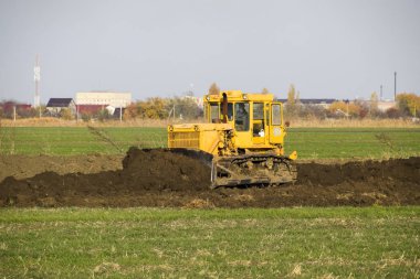 Sarı traktör ekli grederom ile zemin tesviye yapar. Drenaj sistemi alanında çalışmak.