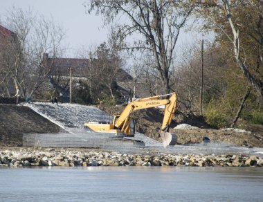 Slavyansk-on-Kuban, Russia - November 8, 2016: Strengthening the embankment of the river in the city. Filling the rubble and leveling the tractor with a scoop. clipart