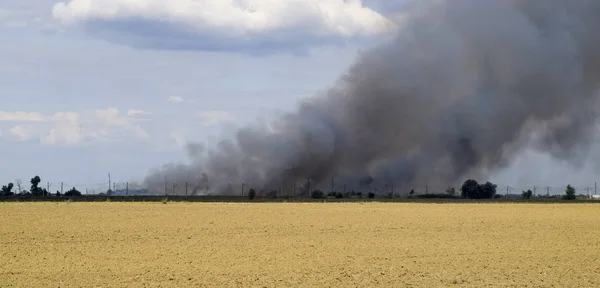 The fire is somewhere beyond the plowed field. Dark smoke from a fire.