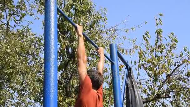 Man trekt zichzelf omhoog op de balk. Sporten in de frisse lucht. Zelfgemaakte horizontale balk in de achtertuin. — Stockvideo