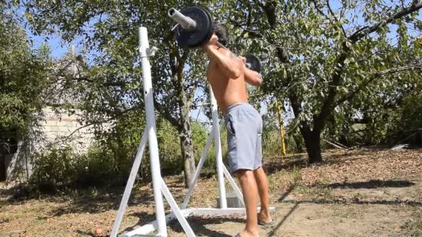 Homme prend un bar pour effectuer des squats. Exercices de musculation. sport dans la cour arrière . — Video