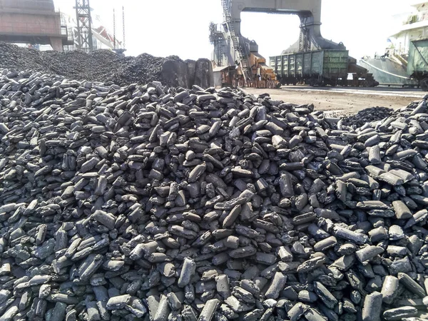 Купи сировинних сталевих брикетів. Купка антрациту вугілля в порту. Портові крани для завантаження вугілля — стокове фото