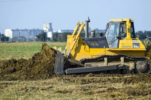 The yellow tractor with attached grederom makes ground leveling. — Stock Photo, Image