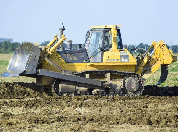 The yellow tractor with attached grederom makes ground leveling. — Stock Photo, Image
