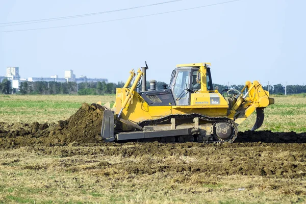 The yellow tractor with attached grederom makes ground leveling. — Stock Photo, Image