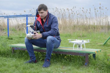 Uzaktan kumanda quadroopter onun elinde olan bir adam bir bankta oturuyor. Beyaz quadroopter hazırlamak için uçuş