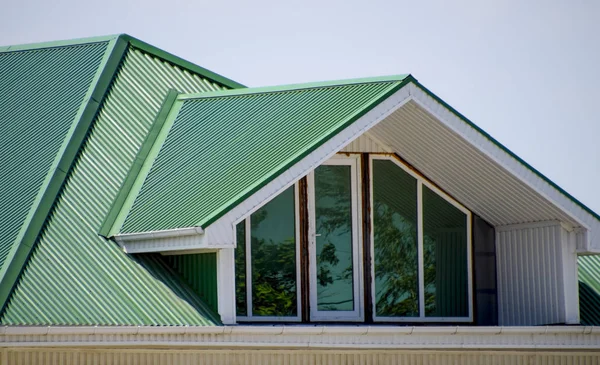 The house with plastic windows and a green roof of corrugated sheet. Green roof of corrugated metal profile and plastic windows.