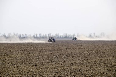 Traktör toprak sahada tırmıklar ve arkasında toz bulutu oluşturur
