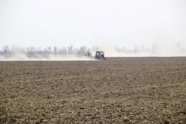 Il trattore erpice il terreno sul campo e crea dietro di esso una nuvola di polvere — Foto Stock