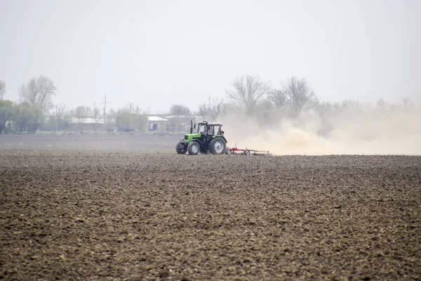 El tractor estrecha el suelo en el campo y crea una nube de polvo detrás de él — Foto de Stock