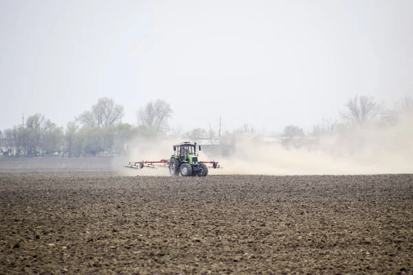 Traktor mengerami tanah di lapangan dan menciptakan awan debu di belakangnya — Stok Foto
