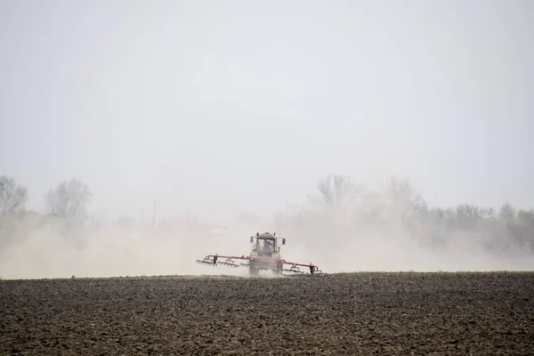 El tractor estrecha el suelo en el campo y crea una nube de polvo detrás de él — Foto de Stock