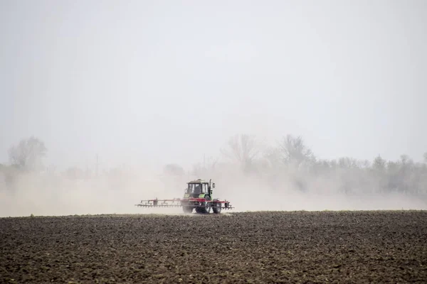 Il trattore erpice il terreno sul campo e crea dietro di esso una nuvola di polvere — Foto Stock