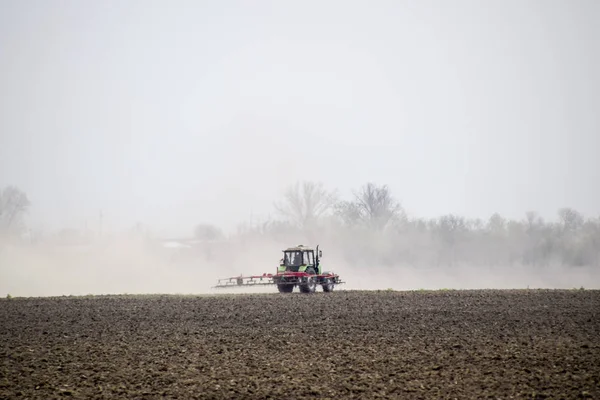 Il trattore erpice il terreno sul campo e crea dietro di esso una nuvola di polvere — Foto Stock