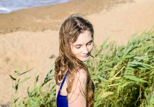 Όμορφη ξανθιά σε ένα μπλε μαγιό σε φόντο πράσινο καλάμια και τη θάλασσα. Το κορίτσι που κοιτάζει προς τα κάτω. — Φωτογραφία Αρχείου