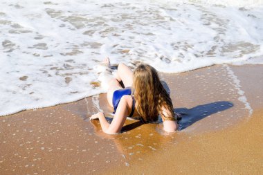 Kız mavi bir mayo içinde sahil üzerinde yatıyor ve rahatlatır. Dalgalar kızlar vücut okşa