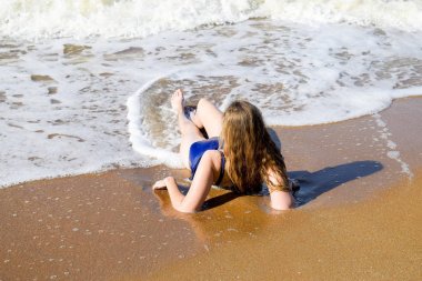 Kız mavi bir mayo içinde sahil üzerinde yatıyor ve rahatlatır. Dalgalar kızlar vücut okşa