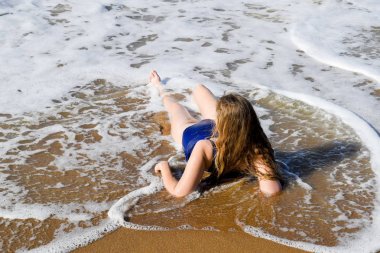 Kız mavi bir mayo içinde sahil üzerinde yatıyor ve rahatlatır. Dalgalar kızlar vücut okşa