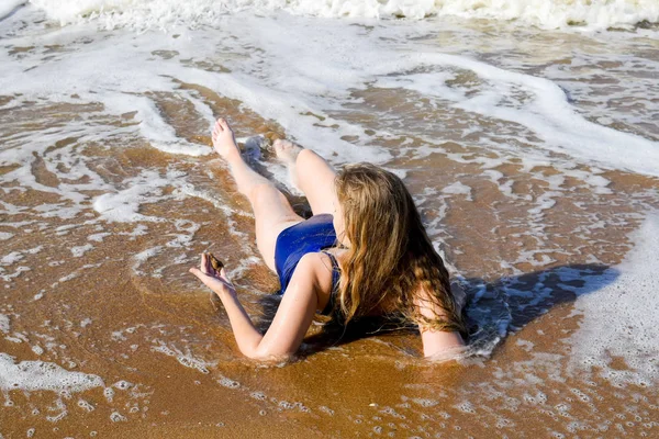 Девушка в синем купальнике лежит на берегу моря и расслабляется. Волны ласкают женское тело — стоковое фото