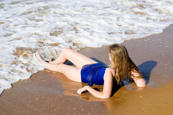 Chica en un traje de baño azul se encuentra en la orilla del mar y se relaja. Olas acarician el cuerpo de las niñas —  Fotos de Stock