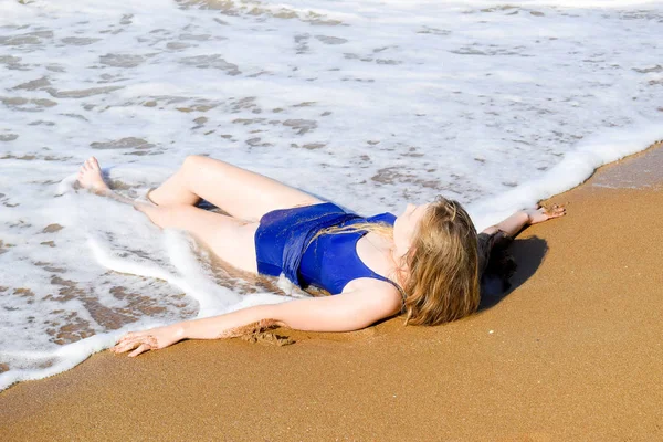 Ragazza in costume da bagno blu si trova sulla spiaggia e si rilassa. Onde accarezzare il corpo delle ragazze — Foto Stock