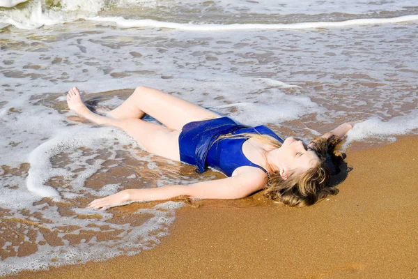Menina em um maiô azul fica na praia e relaxa. Ondas acariciam o corpo das meninas — Fotografia de Stock