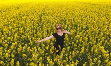 Tecavüz alanında renkleri arasında siyah elbiseli bir kız. Kız sarı çiçekler arasında yürümek. Çiçekli tecavüz.