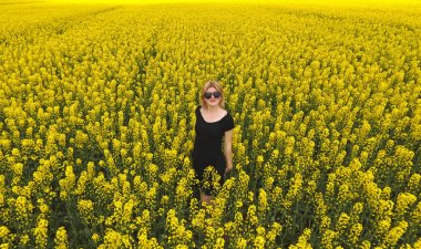 Tecavüz alanında renkleri arasında siyah elbiseli bir kız. Kız sarı çiçekler arasında yürümek. Çiçekli tecavüz.