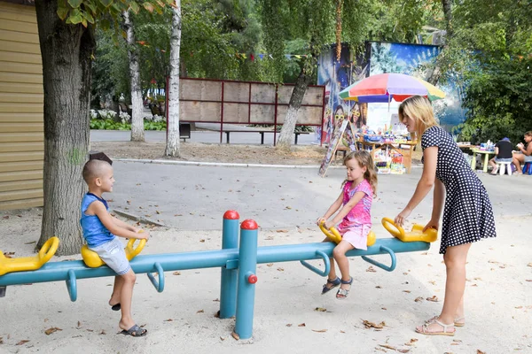 Uma jovem mãe brinca com as crianças no parque infantil . — Fotografia de Stock