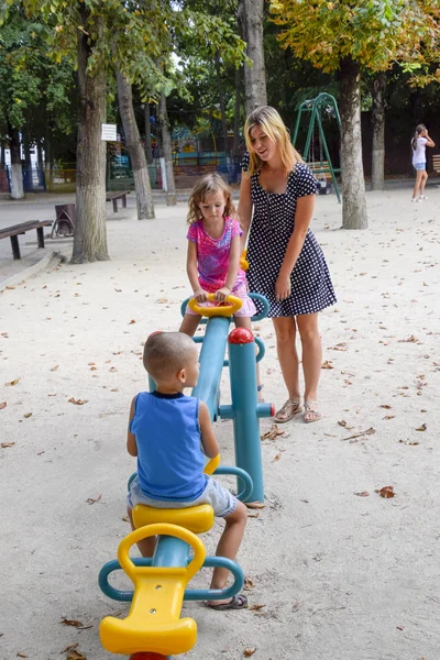 Młoda matka bawi dzieci na placu zabaw. — Zdjęcie stockowe