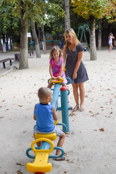 Une jeune mère joue avec les enfants sur l'aire de jeux . — Photo