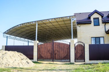 Çitleri ve kapıları olan tuğladan bir ev. Çelik bir tente. 