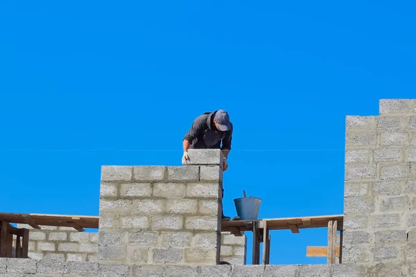 Stavitel staví zeď domu z tvárnicového špalku. — Stock fotografie