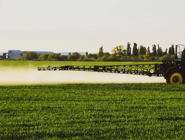 Traktor s pomocí postřikovače rozstřikuje tekutá hnojiva na mladou pšenici na poli. — Stock fotografie