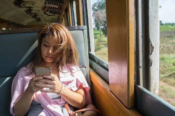 Thai kvinna som tittar på mobiltelefon på rörliga tåg — Stockfoto