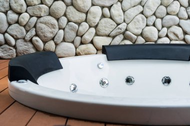 Empty white whirlpool bathtub with stone wall background clipart
