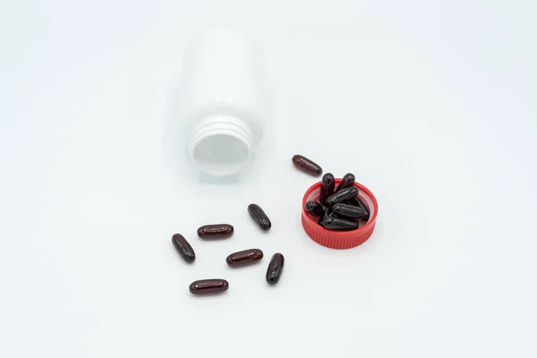 Cápsulas negras, tapa roja y frasco blanco sobre fondo blanco — Foto de Stock