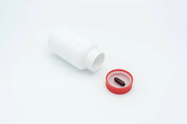 Cápsula preta na tampa vermelha do frasco e no frasco branco aberto — Fotografia de Stock