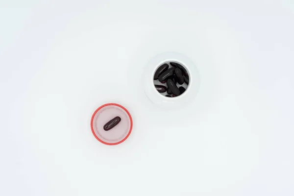Cápsulas negras en tapón rojo y frasco blanco — Foto de Stock