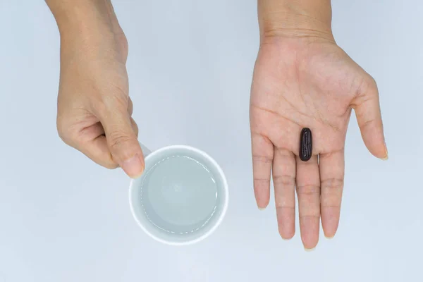 Manos femeninas sosteniendo taza de agua y cápsula negra — Foto de Stock