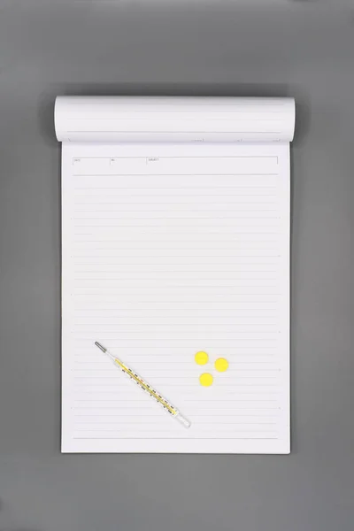 Píldoras amarillas y termómetro sobre papel blanco en blanco — Foto de Stock