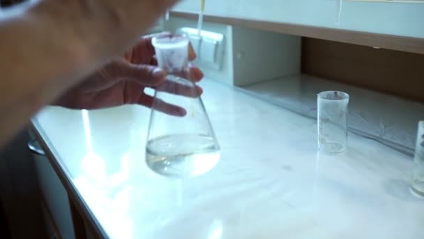 Händer i handskar mixar rosa flytande och gul vätska i kolven i lab — Stockvideo