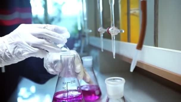 Τα χέρια με γάντια αναμιγνύει ροζ υγρά και κίτρινο υγρό στη φιάλη στο εργαστήριο — Αρχείο Βίντεο