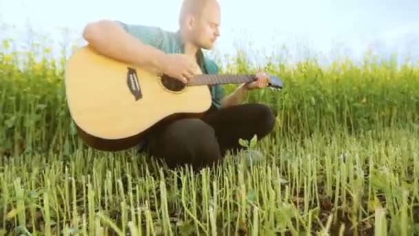 Junger Mann, der auf einem Feld eine Ukulele spielt, singt energisch, in Zeitlupe — Stockvideo