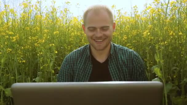 Jovem de óculos sentado na grama e digitando no laptop — Vídeo de Stock