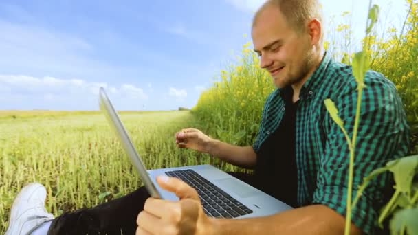 Young man in glasses sitting on the grass and typing on the laptop — Stock Video