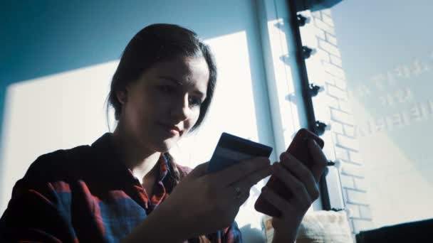 Sorridente giovane donna seduta a tavola utilizzando touchpad e tenendo in mano la carta di credito — Video Stock