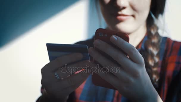 Mujer joven sonriente sentada en la mesa usando touchpad y sosteniendo la tarjeta de crédito en su mano — Vídeos de Stock
