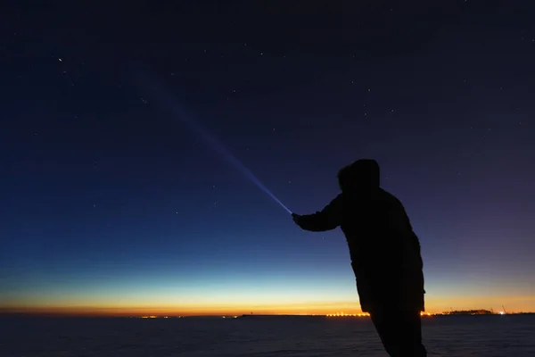 Silhouette of a man with a flashlight, observing beautiful, wide blue night sky with stars and visible Milky way galaxy. Astronomy, orientation, clear sky concept and background.